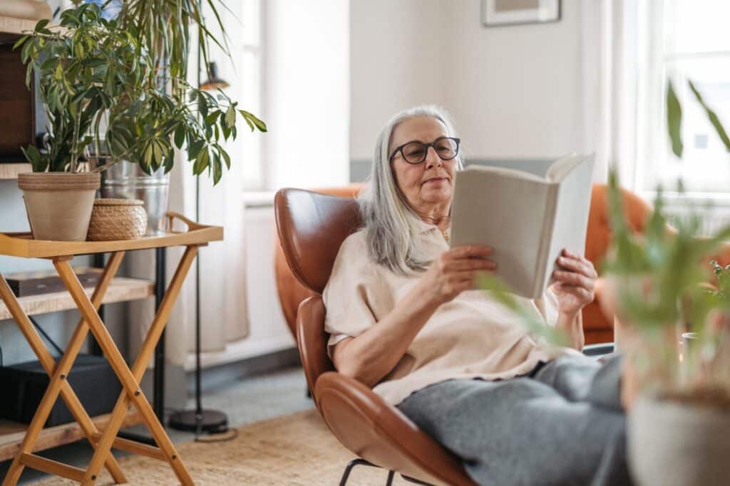 Senior woman reading book, enjoying time alone in her apartment.